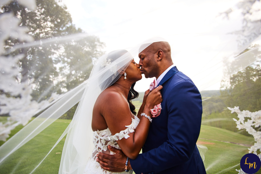 couple kissing beneath bride's wedding veil blowing in the wind