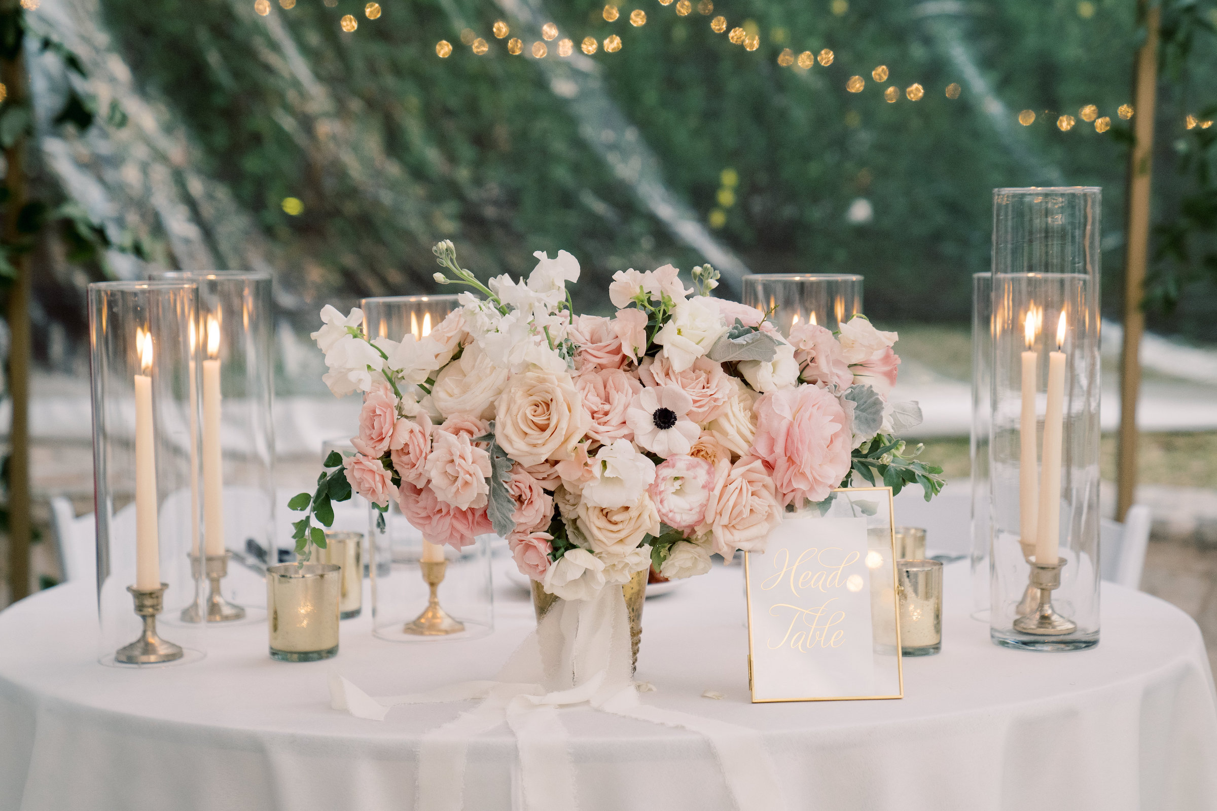tablescape with pink and white florals among glass votives with glowing tall white candlesticks