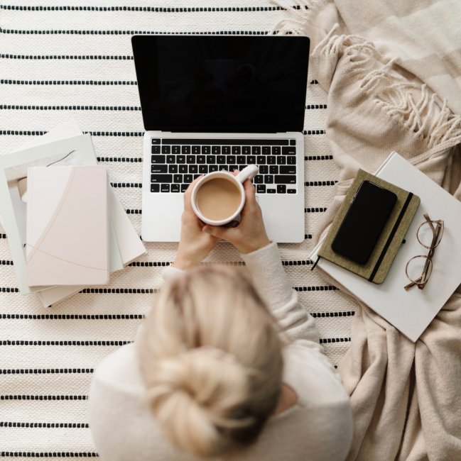 woman with coffee and blond haired bun working on the floor with her computer